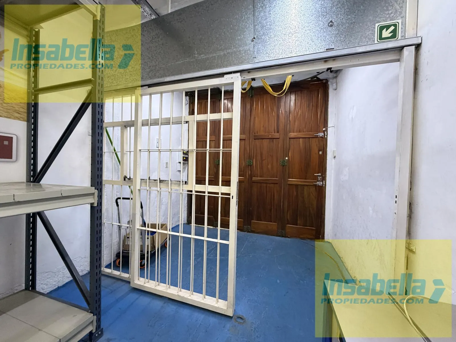 Acceso de carga y descarga al fondo del local, con reja de seguridad y portón de madera